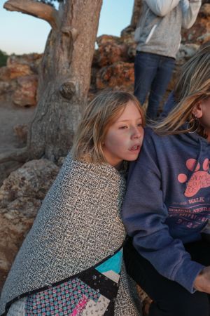 People relaxing against stone ruins while wrapped in a patterned blanket during sunset.
