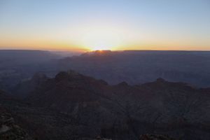 Panoramic view of a desert canyon landscape at sunset with layered mountain silhouettes.