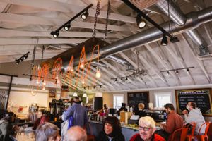 Interior of a busy restaurant with exposed ceiling pipes and hanging orange decorations.