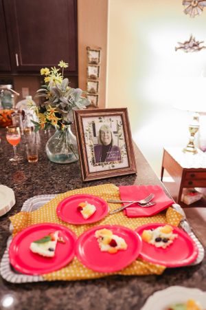 A party table setting with pink plates, floral centerpiece and framed photo on granite countertop.