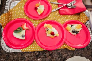 Pink party plates with food arranged on polka dot placemat on dark granite counter.