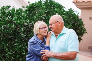 Senior couple sharing a tender moment together outdoors with green foliage in the background.