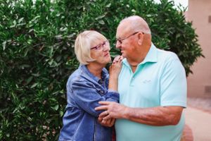 Romantic elderly couple embracing in a garden setting with lush greenery.
