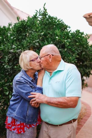 Affectionate senior couple in casual attire sharing a sweet moment against green landscaping.