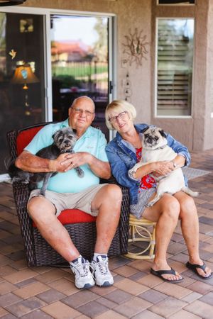 Senior couple relaxing on patio furniture with small dogs on their laps.