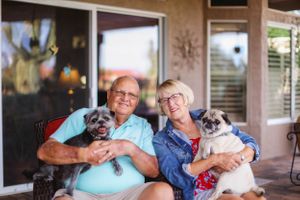 Elderly couple sitting on outdoor patio furniture with their pet pug.