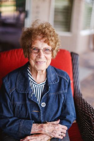 A person in a denim jacket and glasses sits comfortably in an outdoor chair.