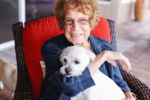 A person in denim shares a joyful moment with a small white dog on a patio.