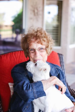 A person cuddles with a fluffy white dog while relaxing in an outdoor chair.