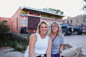 Two people sit together on a curb in front of pink buildings during daytime.