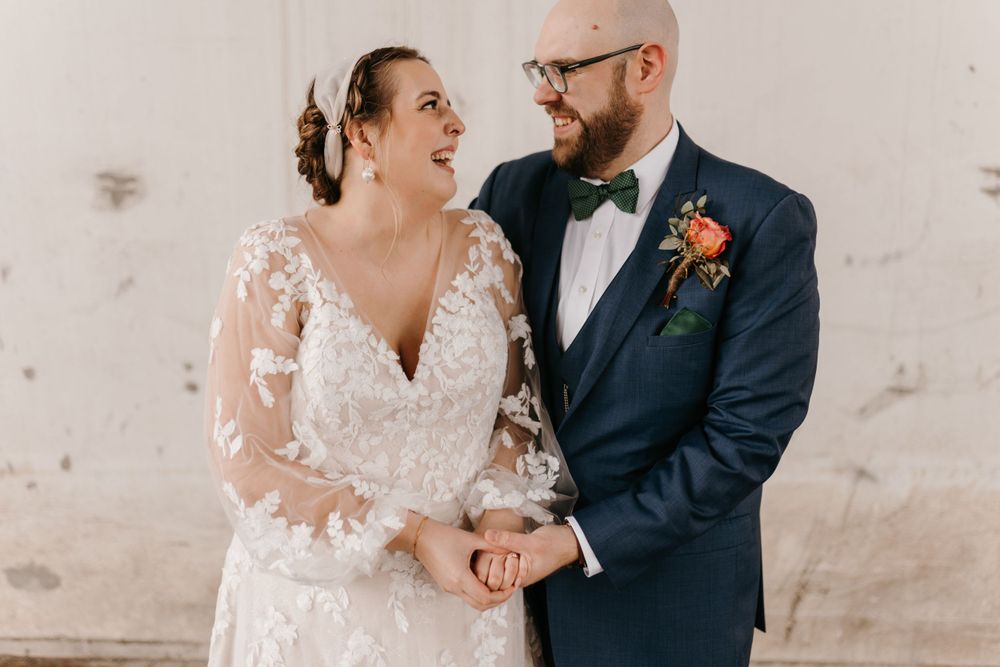 Bride and groom smiling at each other lovingly while holding hands at wedding.