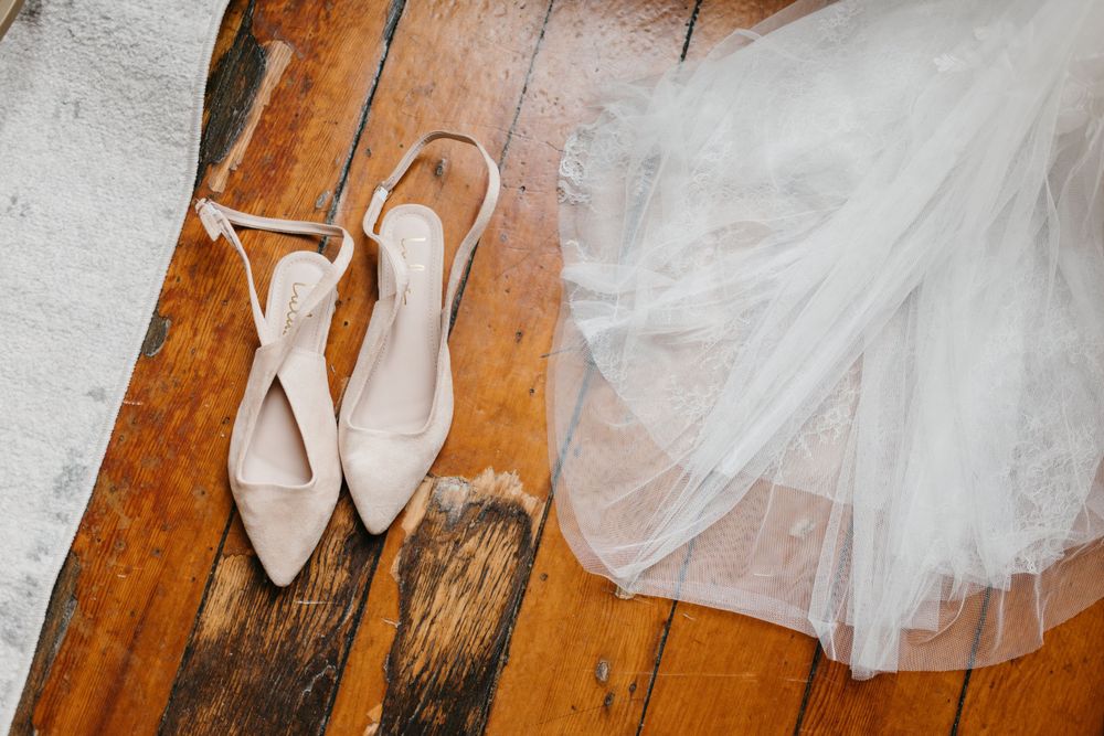 Bridal slingback heels and wedding veil on rustic hardwood floor.