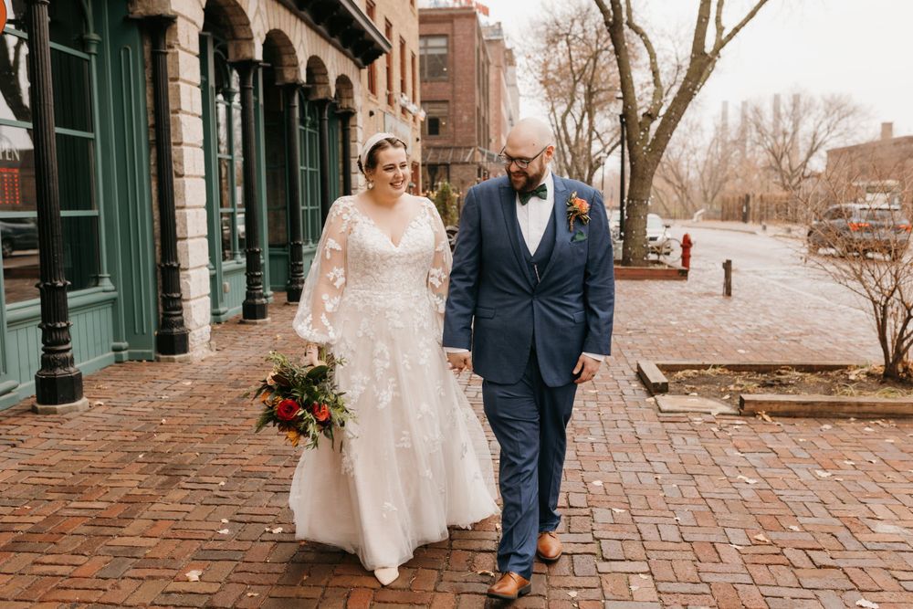 Wedding couple walking together on cobblestone street, bride carrying vibrant fall floral bouquet.