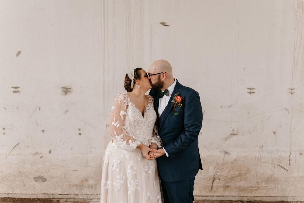 Bride and groom sharing a romantic kiss outdoors in elegant wedding attire.