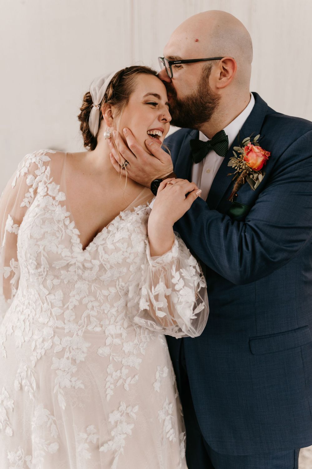 Bride laughing as groom kisses her cheek while holding her face lovingly.