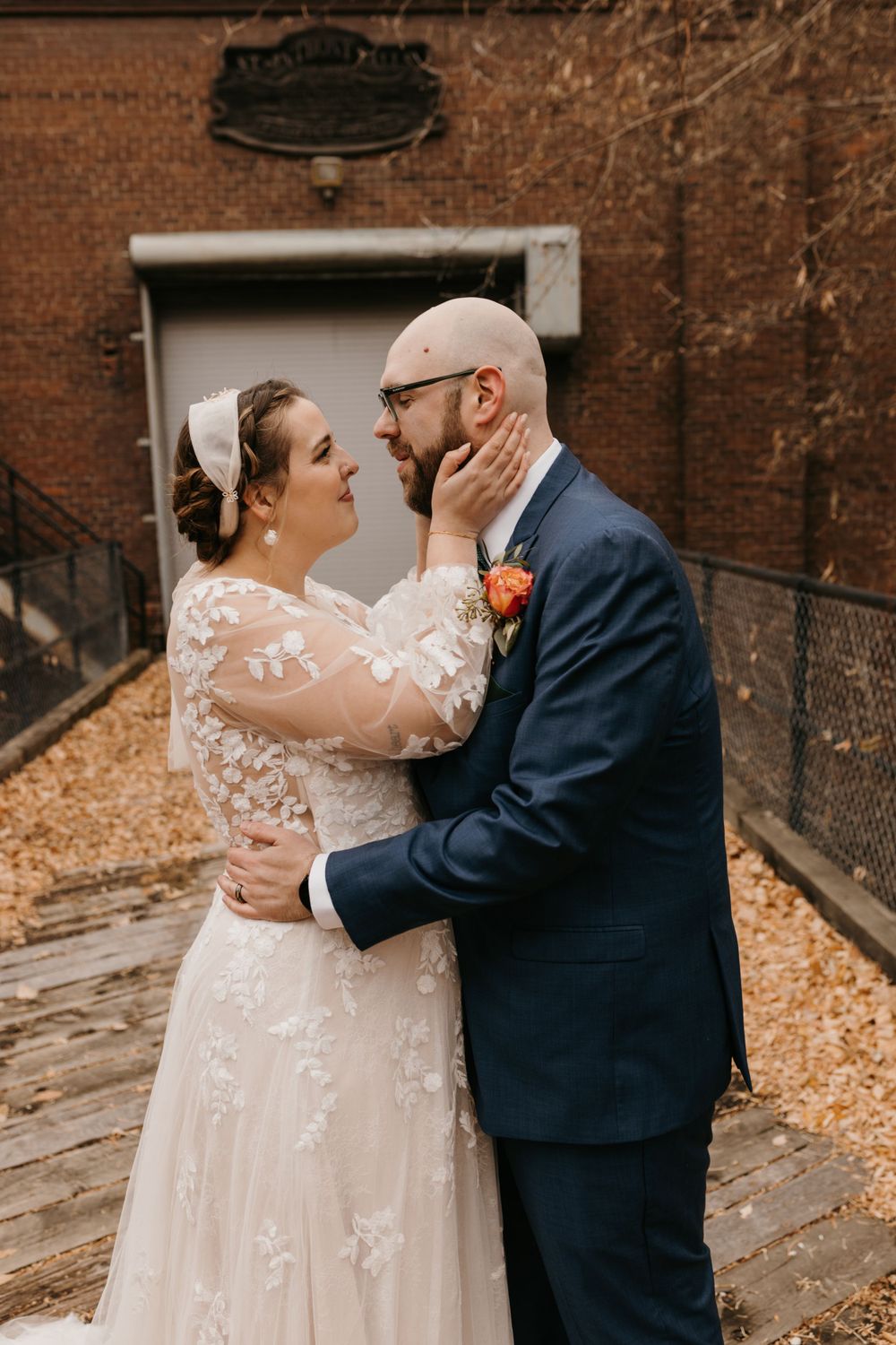 Smiling bride tenderly holds grooms face as they share an intimate moment outdoors.