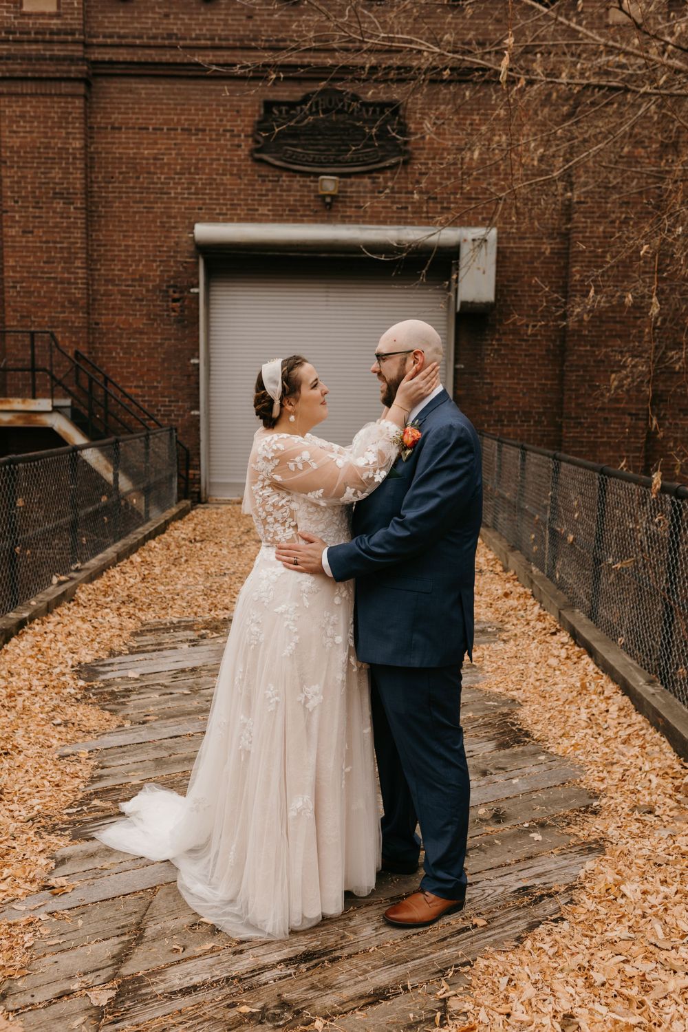 Newlyweds embrace romantically on a wooden walkway surrounded by fallen autumn leaves.