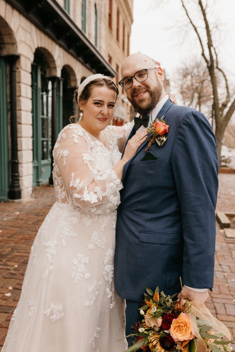 Smiling newlyweds posing together, bride touching groom's lapel, holding autumn floral wedding bouquet.