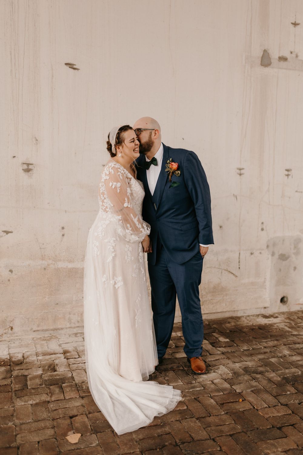 Bride laughing joyfully as groom whispers to her outside rustic brick venue.