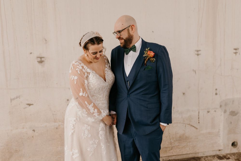 Bride and groom smiling at each other holding hands in elegant wedding attire.