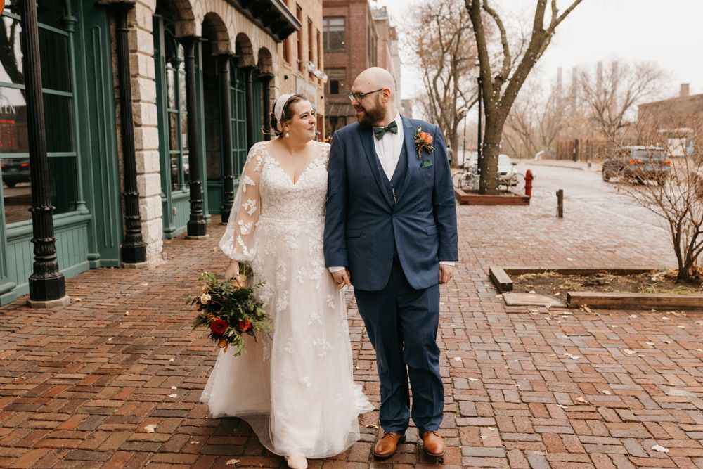 Bride and groom holding hands while walking along charming brick-paved historic district street.
