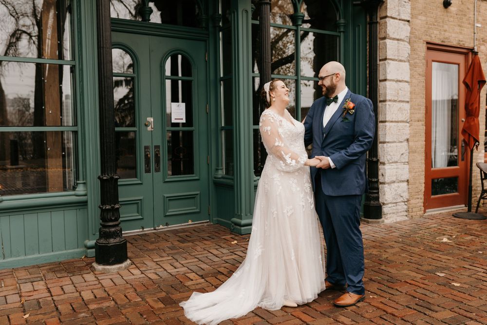 Bride and groom holding hands and smiling outside green historic building on wedding day.