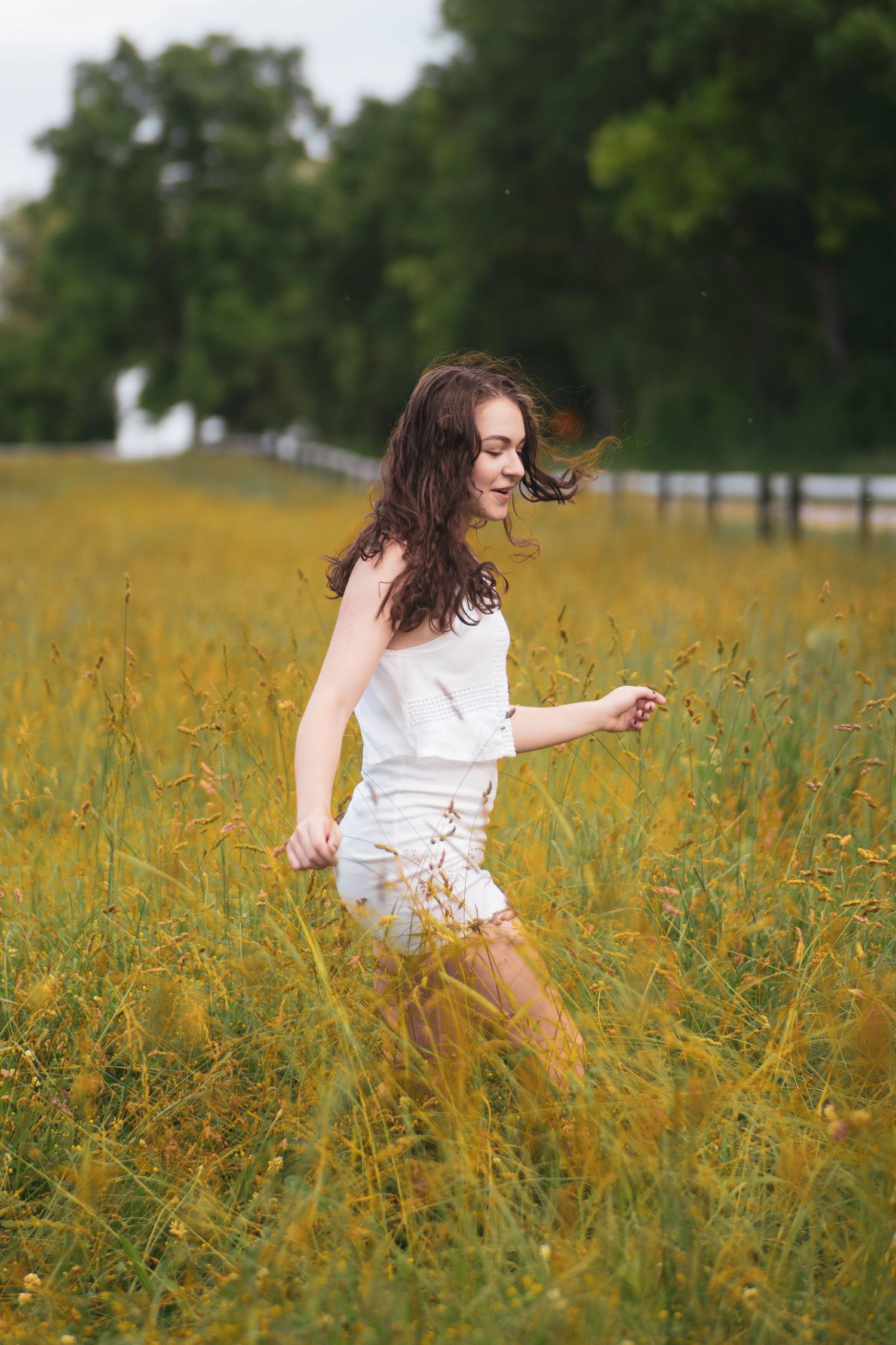 Person in white dress twirls joyfully through a golden field of tall grass and wildflowers.