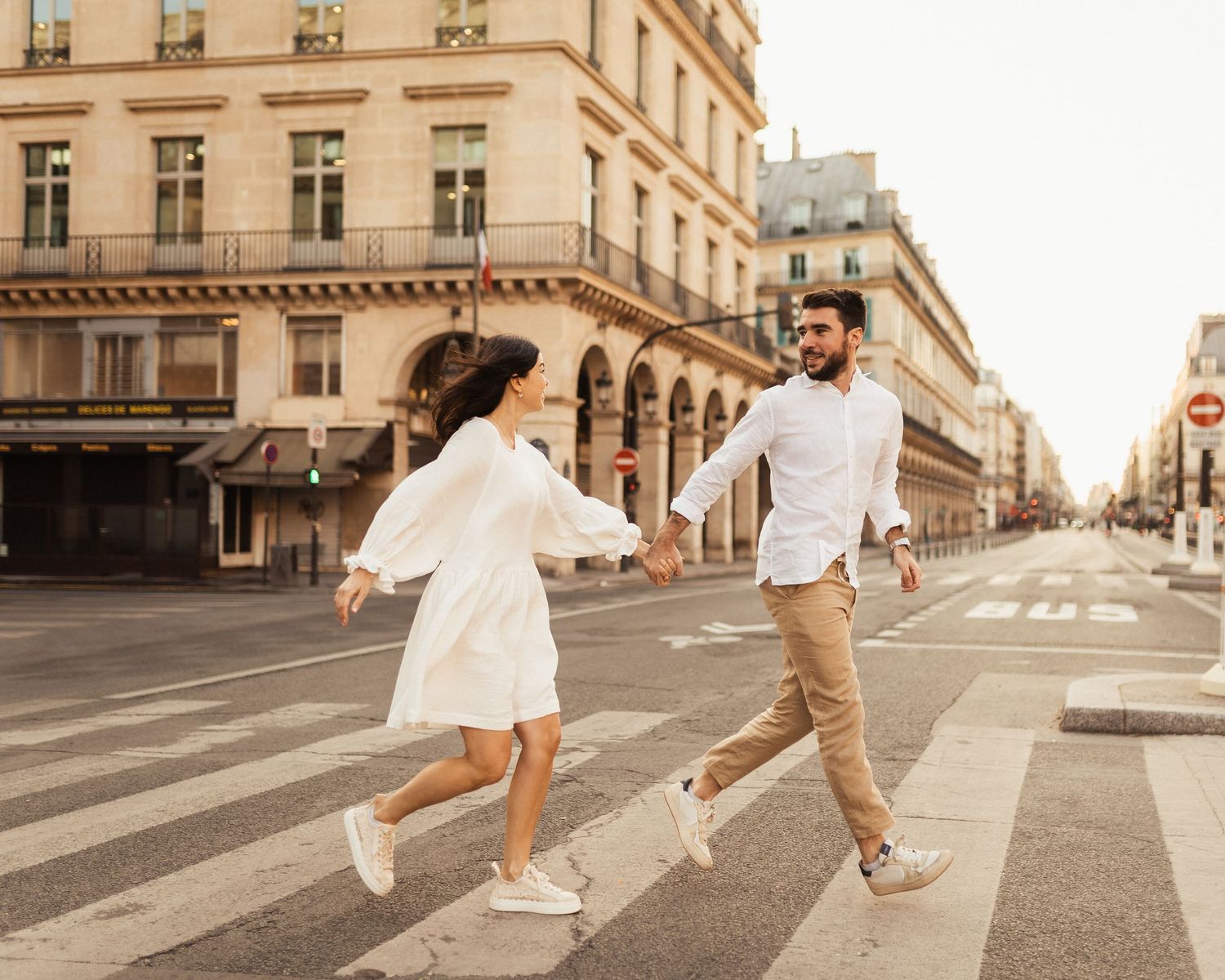 Couple dancing and jumping across Parisian crosswalk in romantic engagement photo.