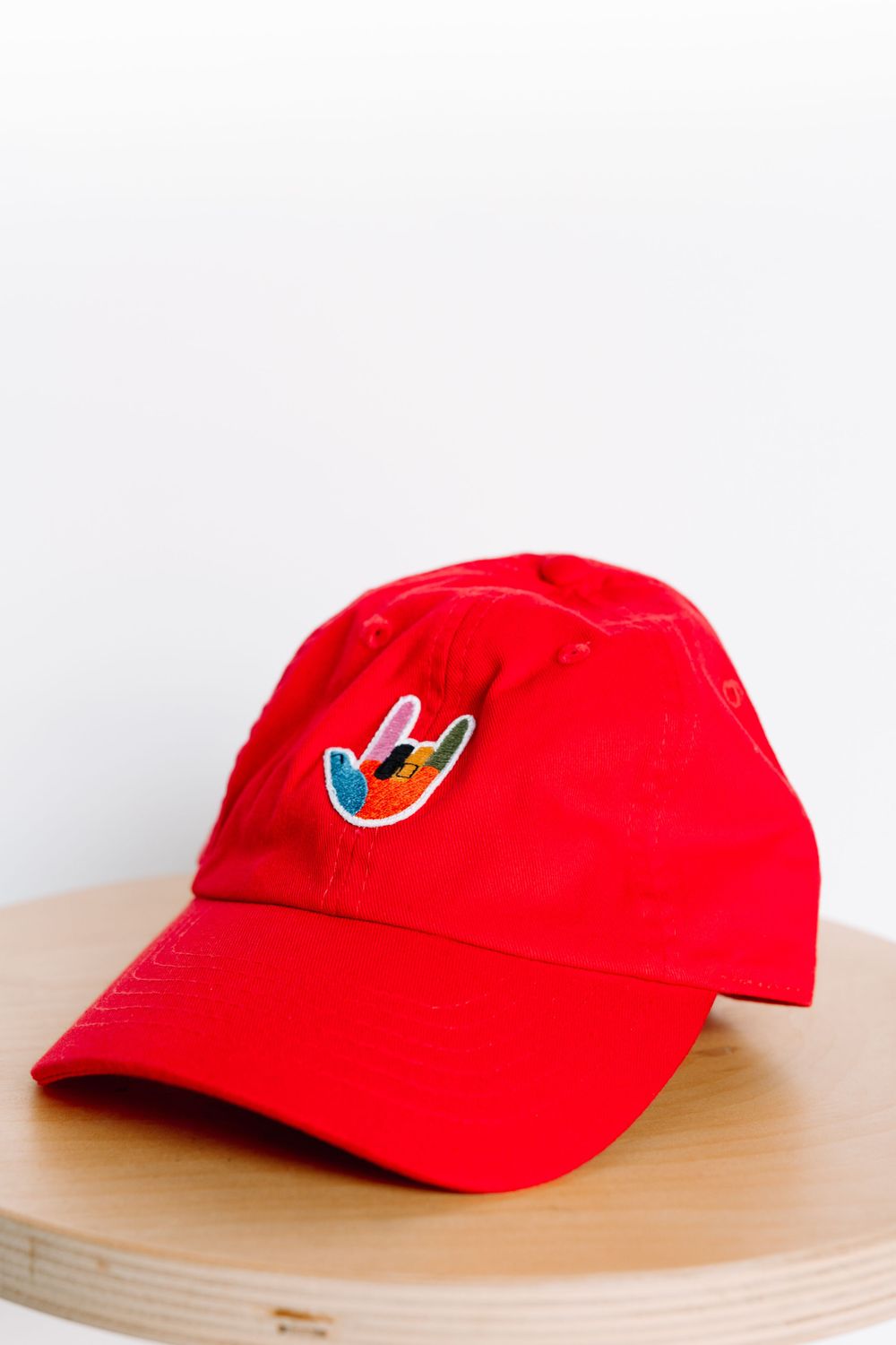 Red baseball cap with small colorful embroidered patch displayed on wooden surface.