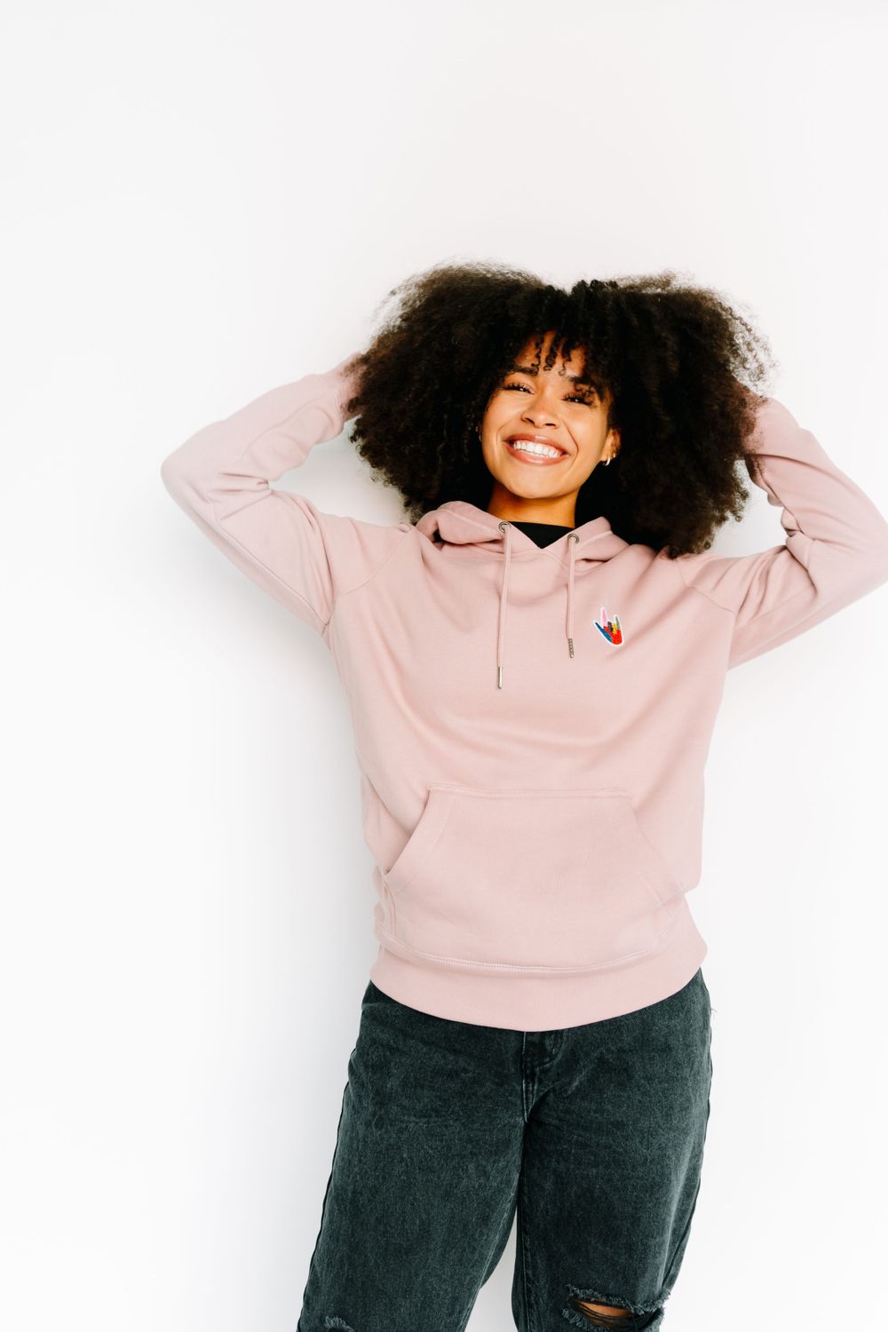 Person wearing pink hoodie and jeans poses playfully against white background.