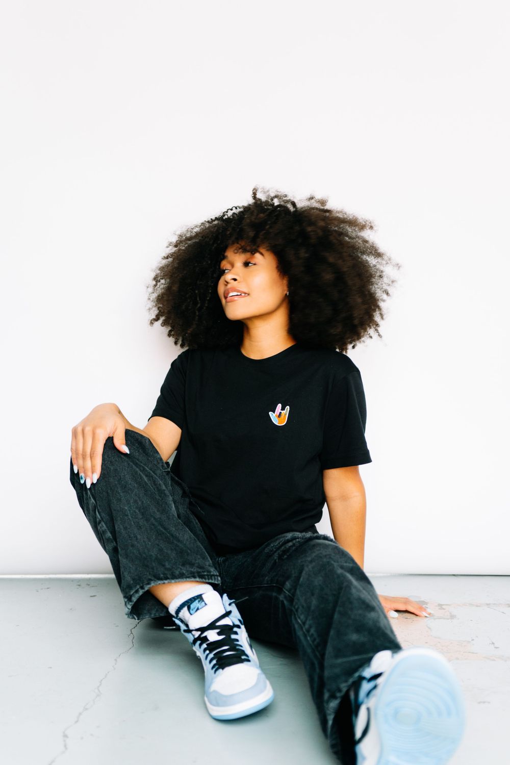 Model wearing black t-shirt and jeans poses casually against white background in studio.
