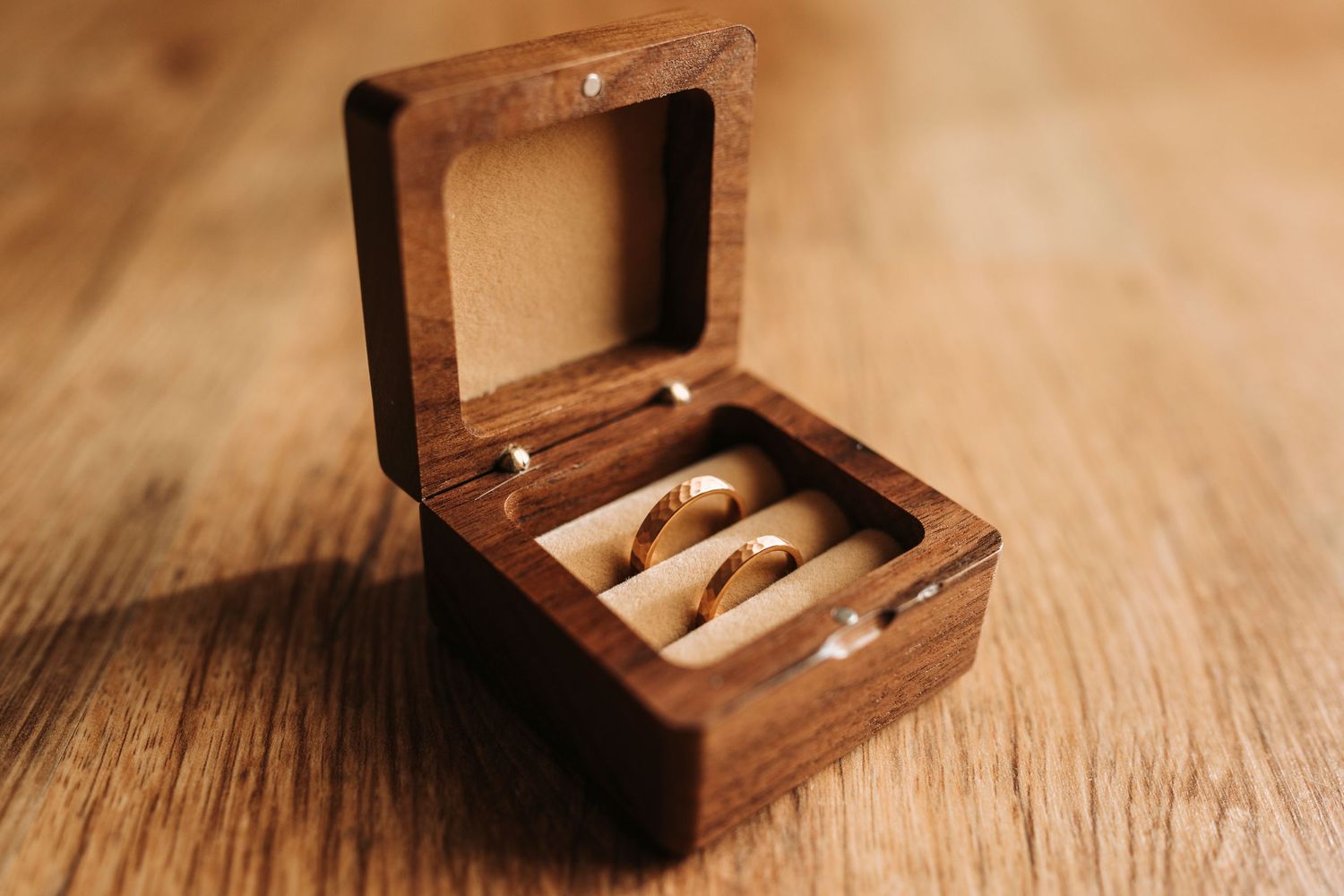 Wedding rings displayed in a small wooden box on rustic wooden surface.