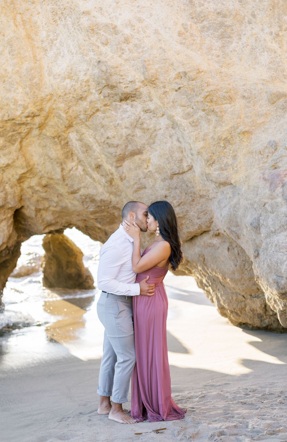 Loving couple shares intimate moment under natural rock arch at scenic beach.