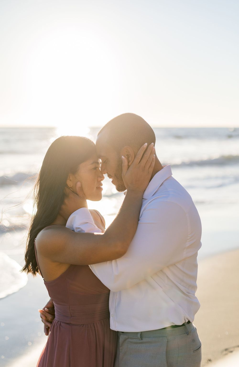 Sunset beach portrait of couple in romantic embrace with ocean waves behind them.