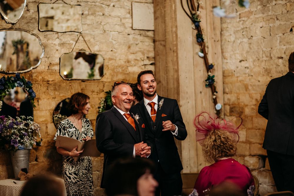 Joyful candid moment during wedding ceremony in rustic stone venue with warm lighting.