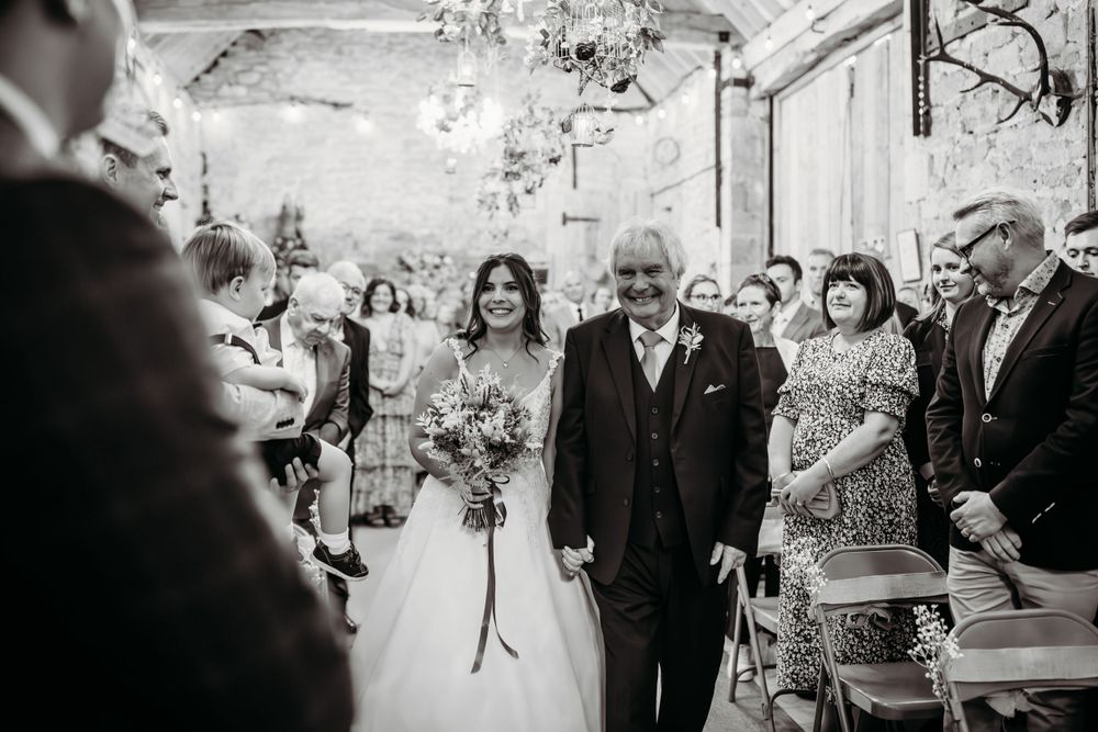 Black and white candid wedding ceremony photo in rustic stone venue with decorative lighting.