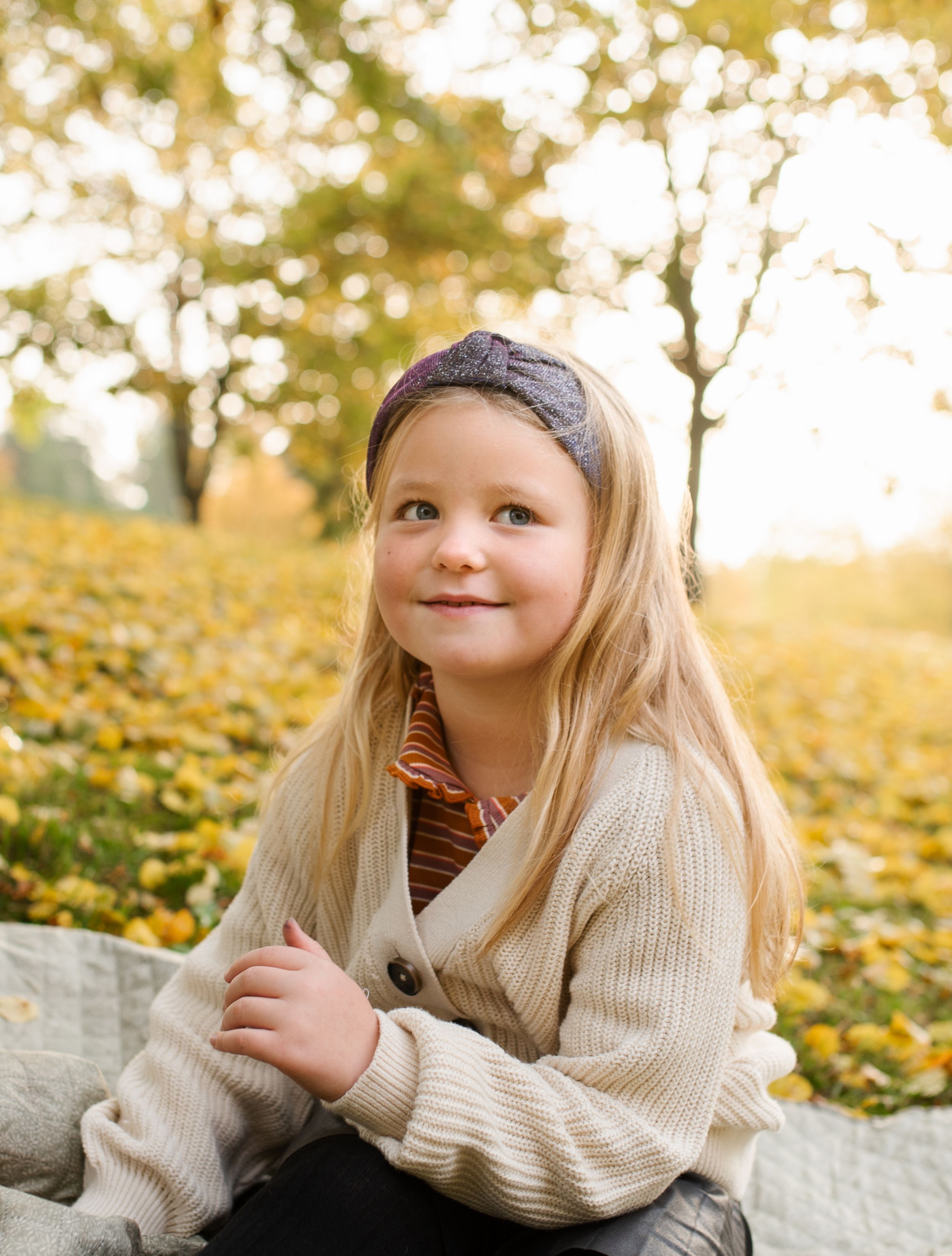 Young person wearing a cream cardigan sitting outdoors in autumn scenery.