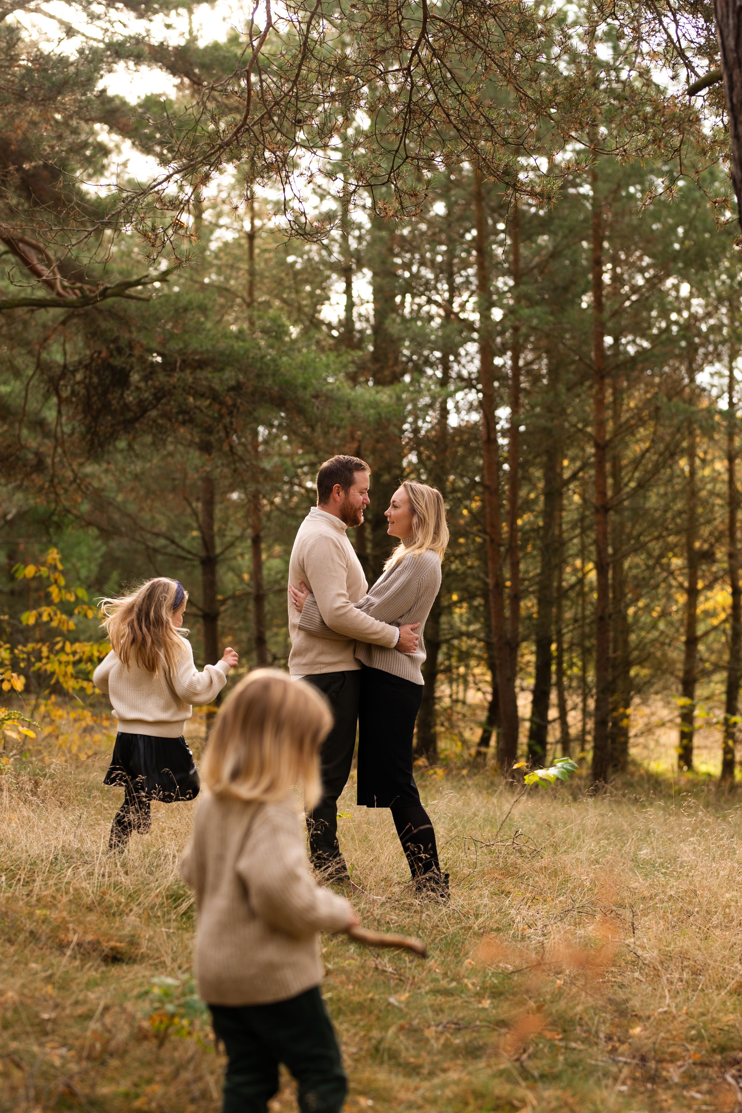 Family enjoying a playful moment together in a pine forest during autumn.