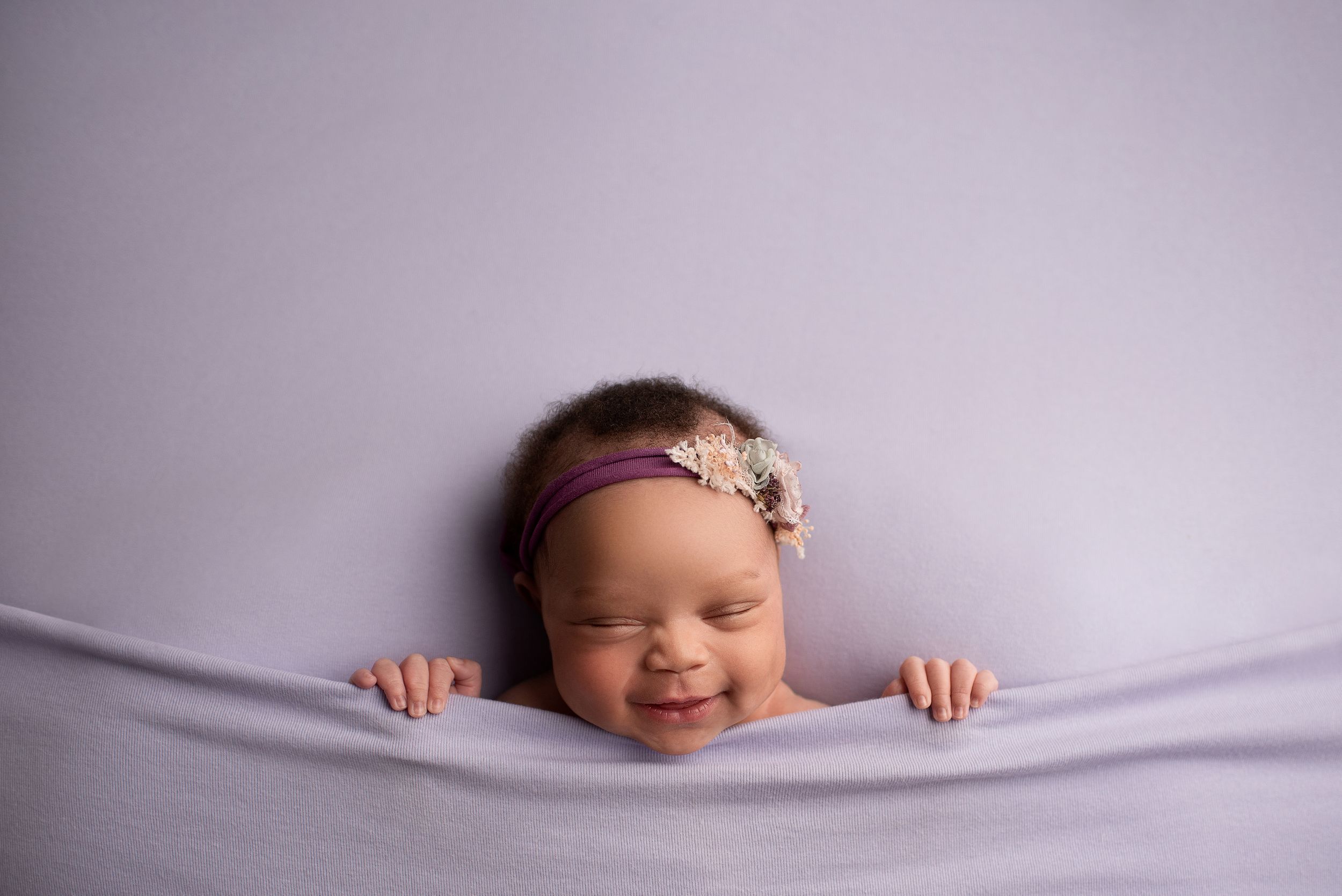 Sleeping, smiling newborn baby girl all tucked in with a lavender blanket