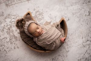 Wrapped newborn boy sleeping in a wooden moon shaped prop with a light tan floor