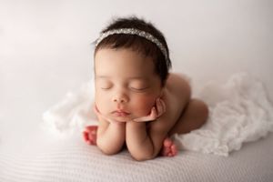Sleeping newborn girl with dark hair in the froggy pose on a ruffled white blanket.