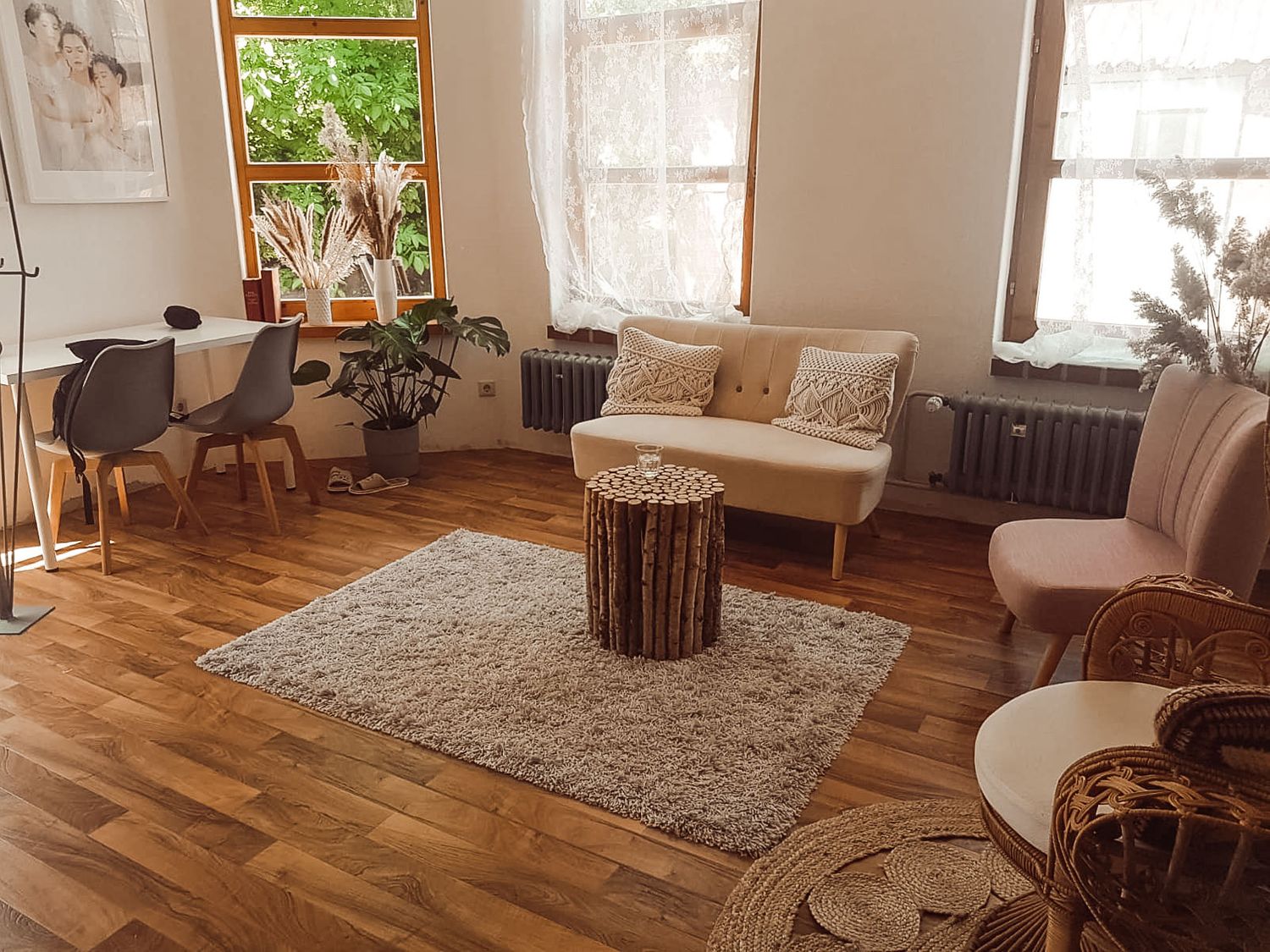 A cozy living room with hardwood floors, beige rug, curved seating, and natural light streaming through windows.