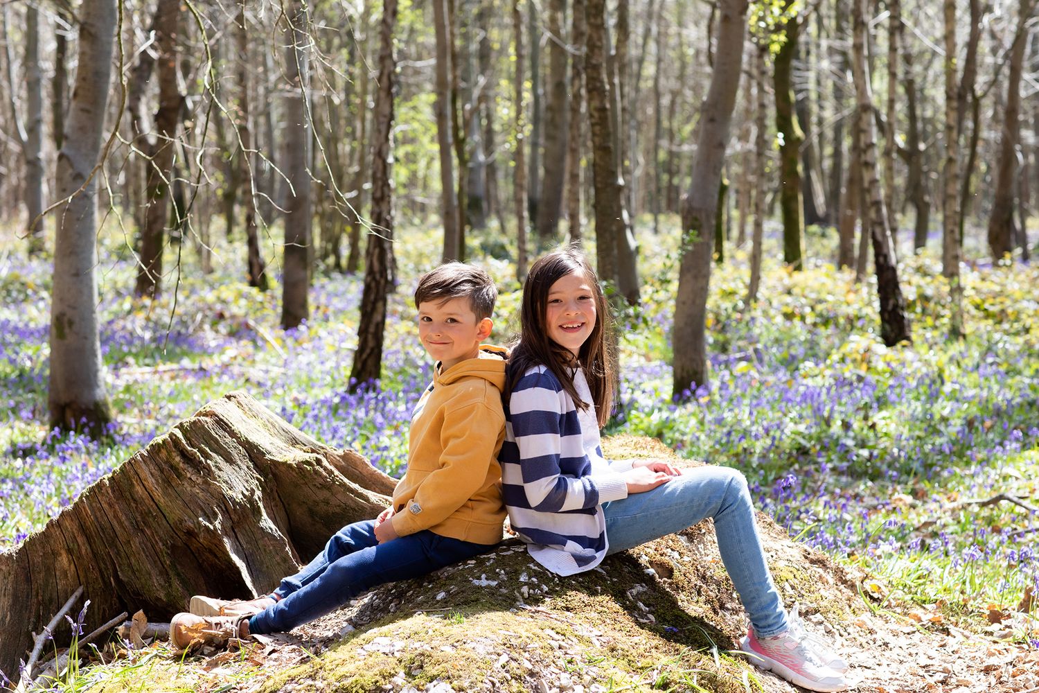 Two people sitting on fallen log in bluebell woodland during spring photo shoot.