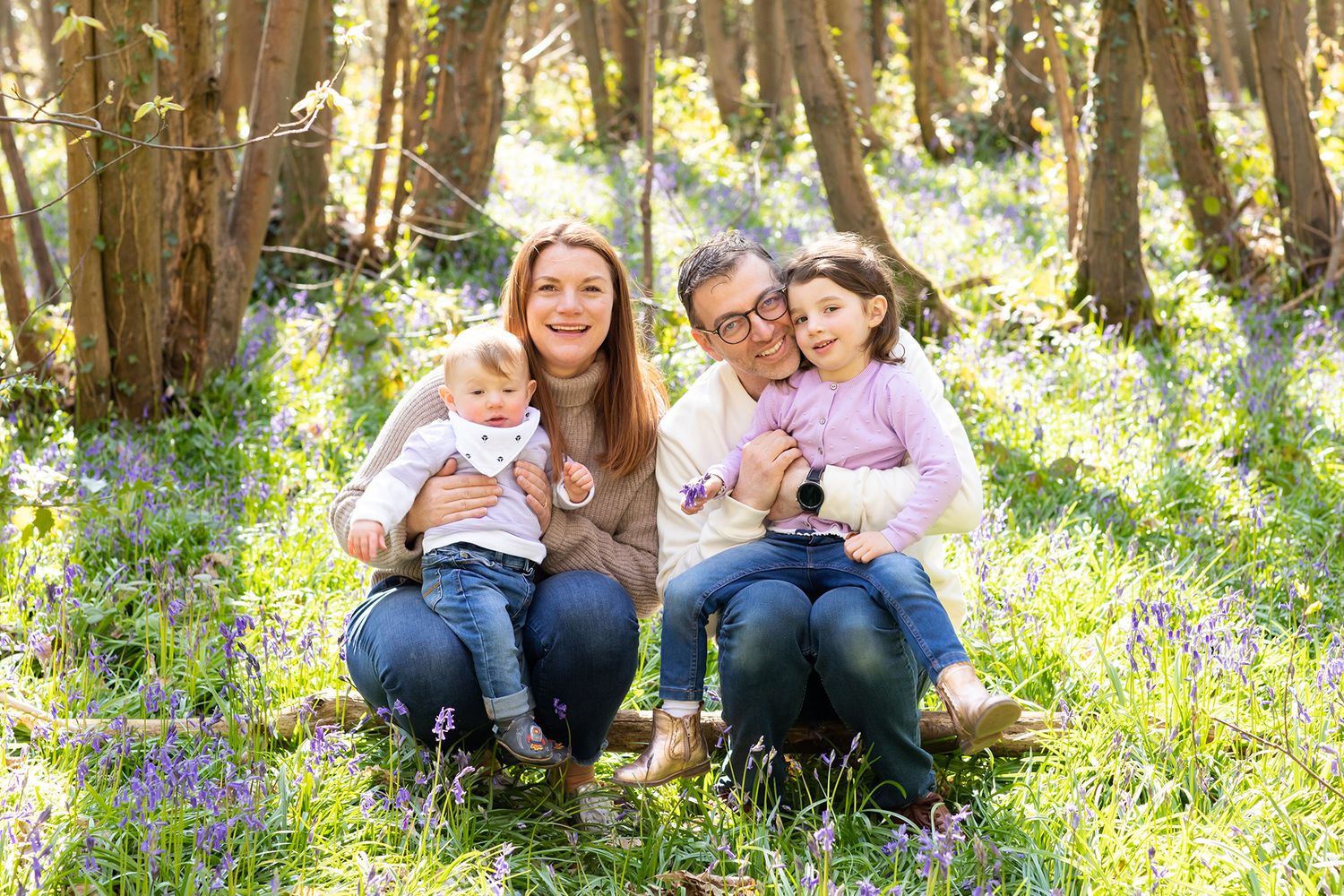 Family sitting in a bluebell woodland during springtime photo session.