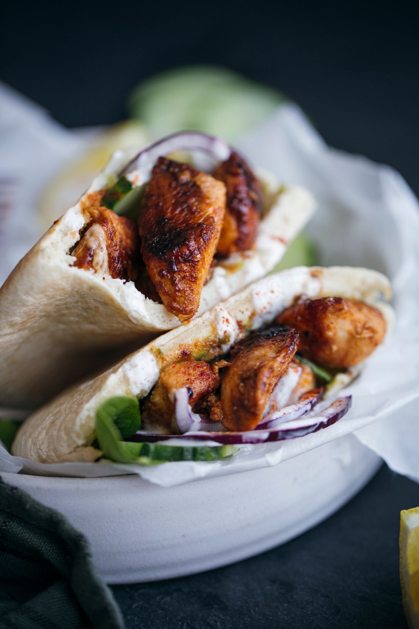 Grilled chicken wrap filled with fresh vegetables and sauce served on white plate.