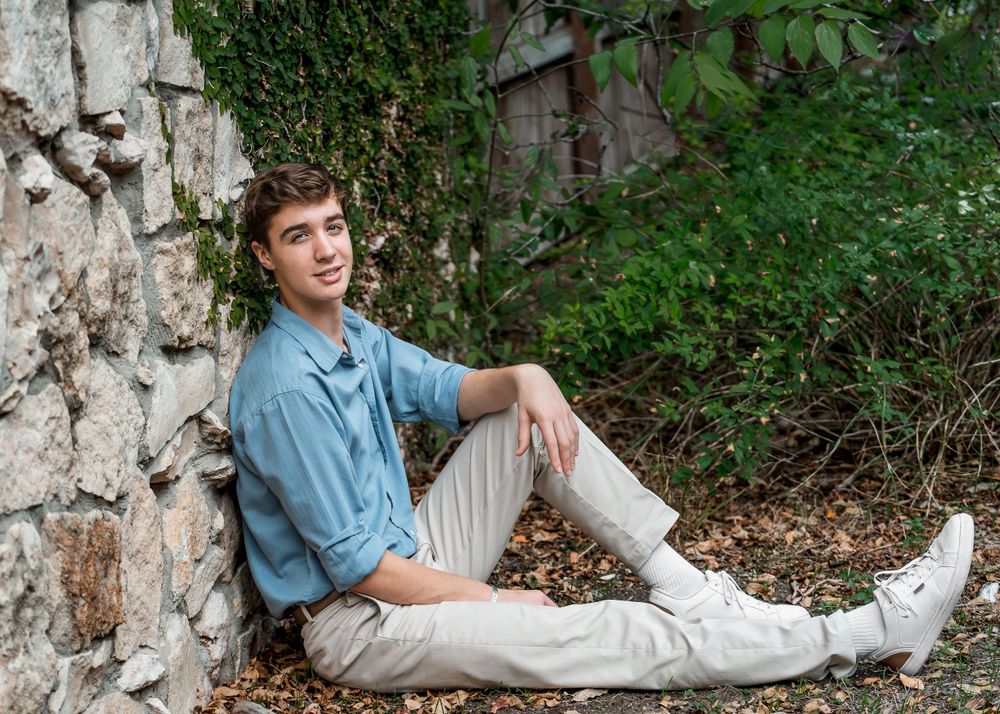 Landa Gardens at Landa Library portrait of high school senior boy in blue shirt sitting against an ivy covered wall