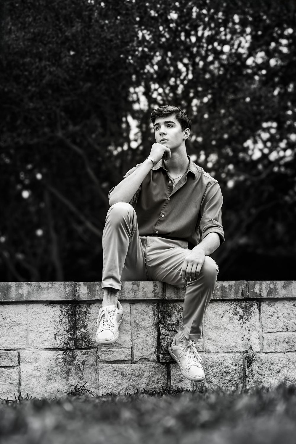 Black and white picture of high school senior boy sitting in Thinker Pose at Landa Gardens iat Landa Library
