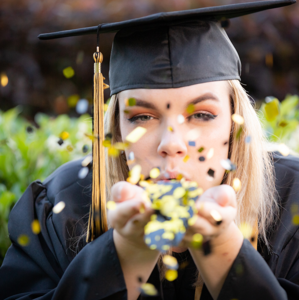 Cap and gown blowing confetti senior celebration