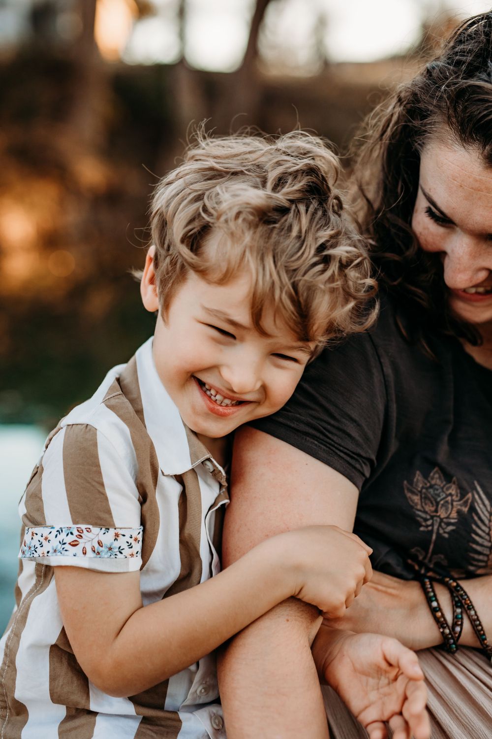 little boy smiling holding his moms arm