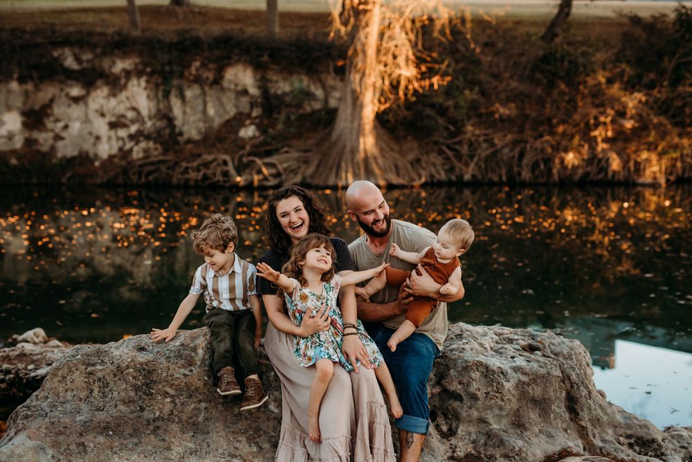 family of five sitting on a big rock by the river